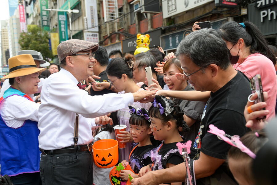 ／新北市長侯友宜身著復古裝扮，帶領變裝民眾一起踩街遊行，沿路發送糖果給小朋友們。（新北市政府經發局提供）